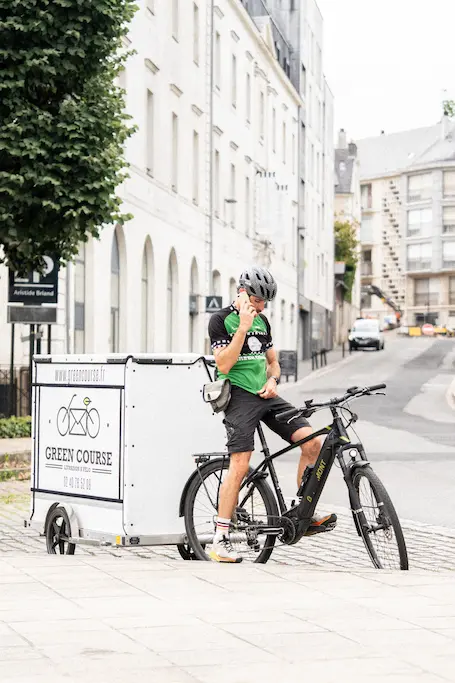 Livreur Green Course au téléphone à côté de son vélo dans une rue de Nantes